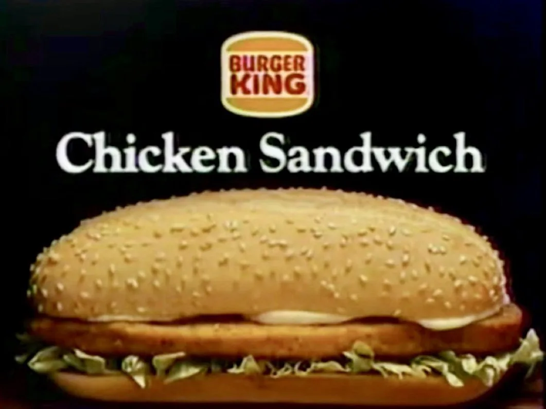 A vintage Burger King advertisement featuring a close-up of their chicken sandwich on a sesame seed bun with lettuce and…