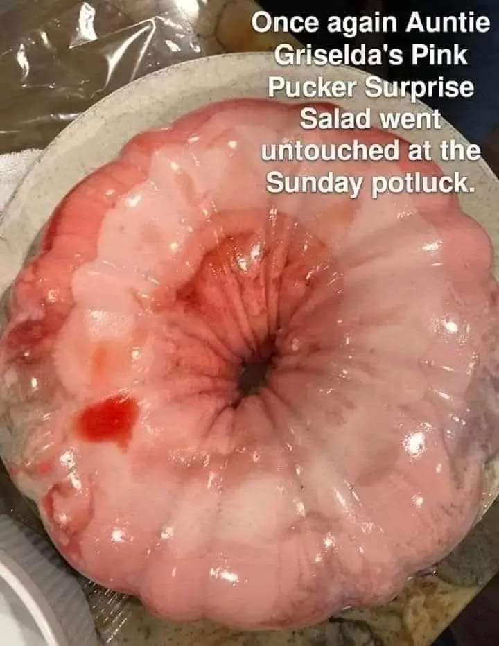 A close-up photo shows a pink, gelatinous, ring-shaped dessert or salad in a fluted metal pan, resembling a brain or a…