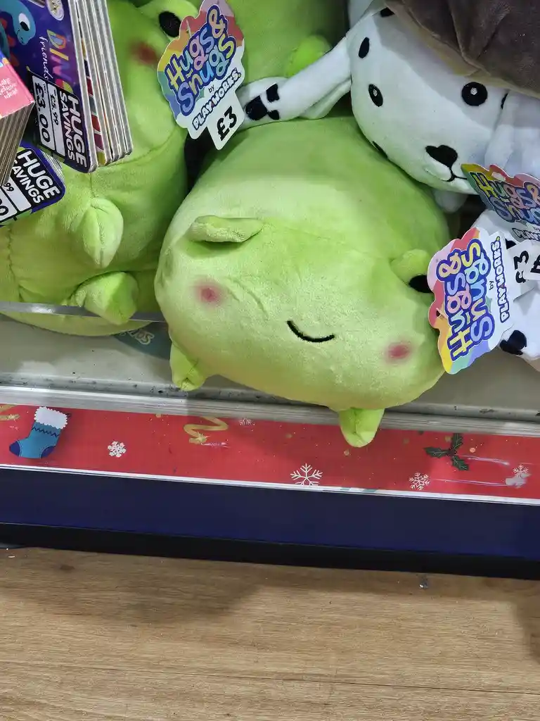 A close-up photo shows a light green, round plush toy with closed eyes and rosy cheeks, appearing to be sleeping or resting…
