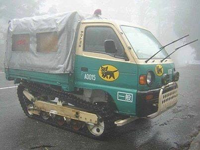 a green and beige tracked vehicle, resembling a small truck or tractor, is shown on a wet road in foggy weather. It has a…