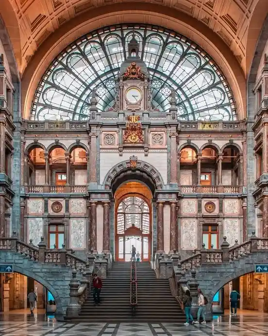 A grand, ornate building interior with a large central staircase leading up to an arched entrance under a massive…