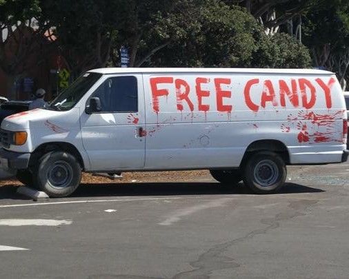 A white van parked in a lot has the words 'FREE CANDY' painted in large red letters across its side, accompanied by red…
