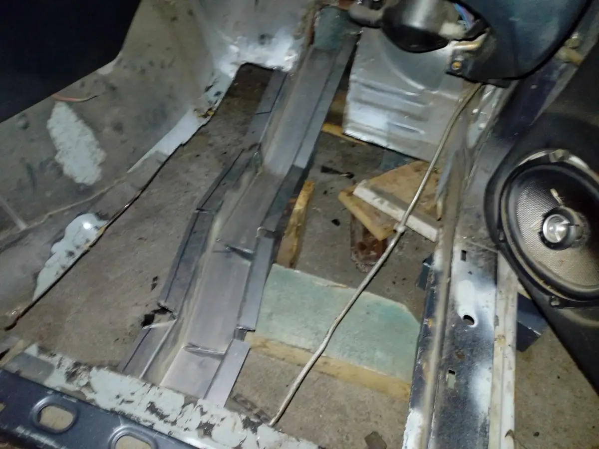 The image shows the interior floor of a car with exposed metal panels, wiring, and a speaker, indicating a car audio…