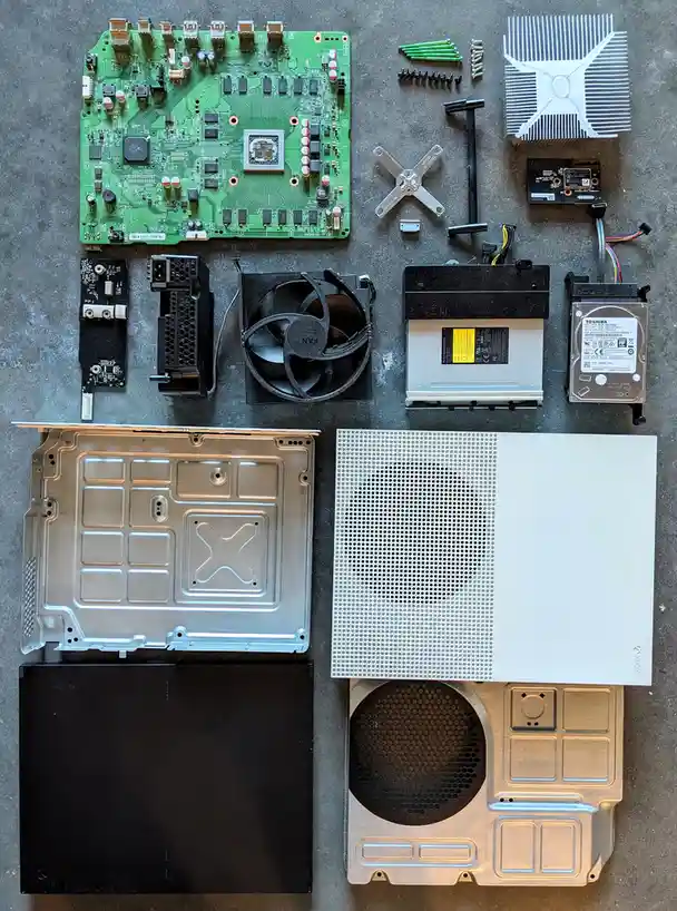An overhead shot displays all the internal components of a disassembled Xbox Series X console laid out on a gray surface…