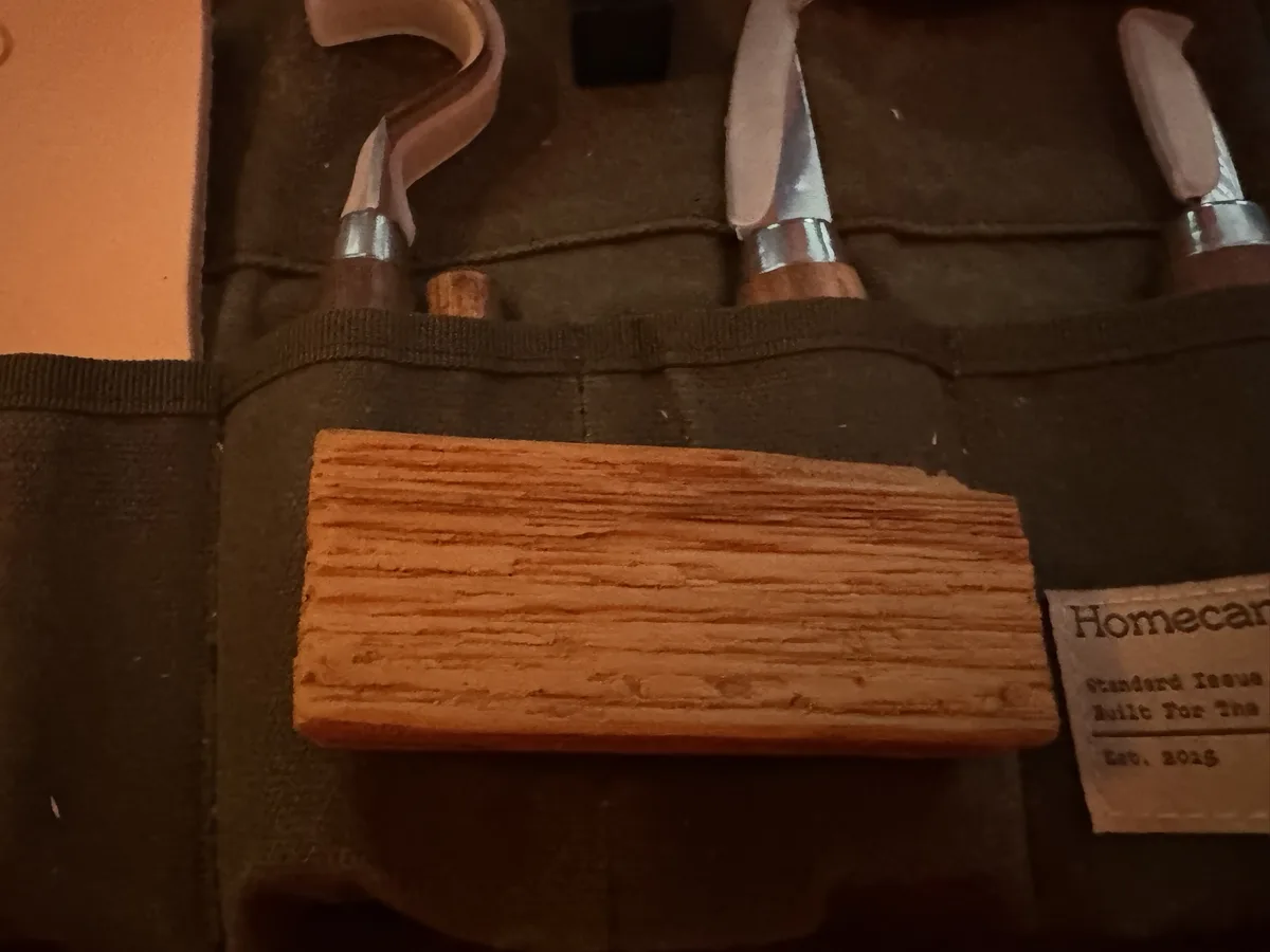A close-up photo shows a wooden block with visible grain resting on a dark green tool roll. Behind it, several woodworking…