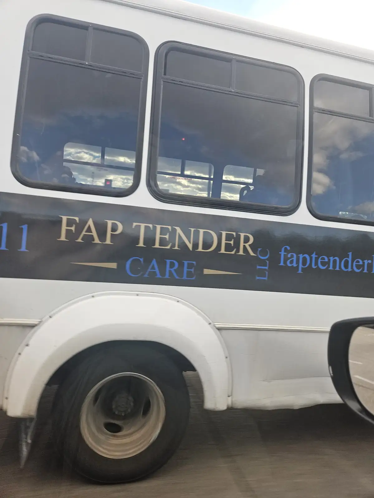 A close-up of a white bus's side shows a dark stripe with the text 'FAP TENDER CARE LLC' in gold and blue lettering. The bus…