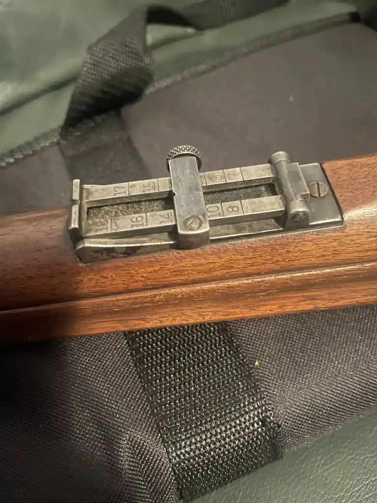 A close-up photo shows the metal safety selector lever of a wooden-stocked rifle, with engraved numbers from 18 down to 1…