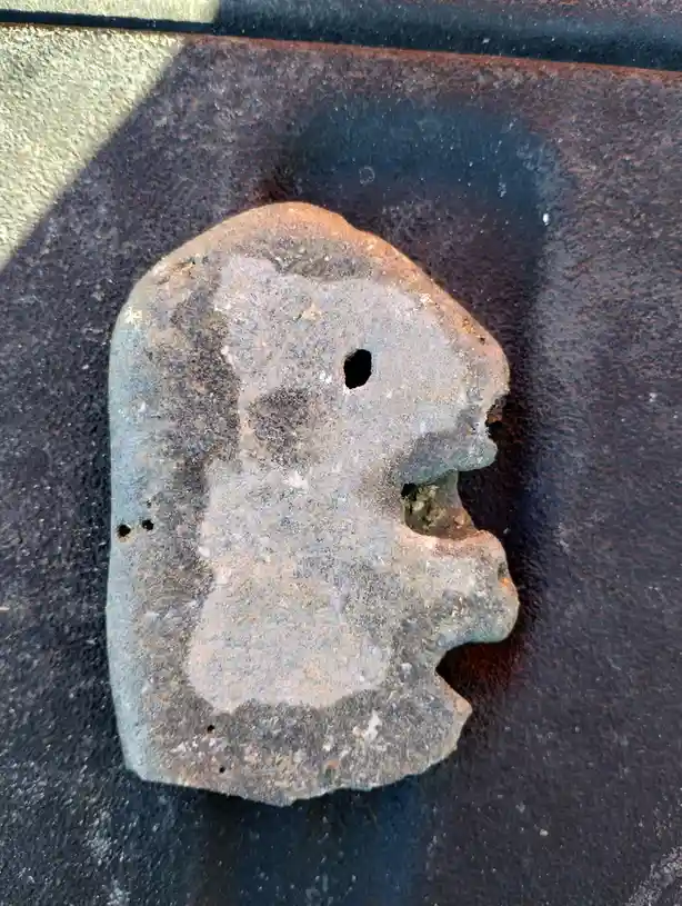 A weathered, rusted metal object shaped like a ghost's head with a hole for an eye and a jagged mouth lies on a rusty…