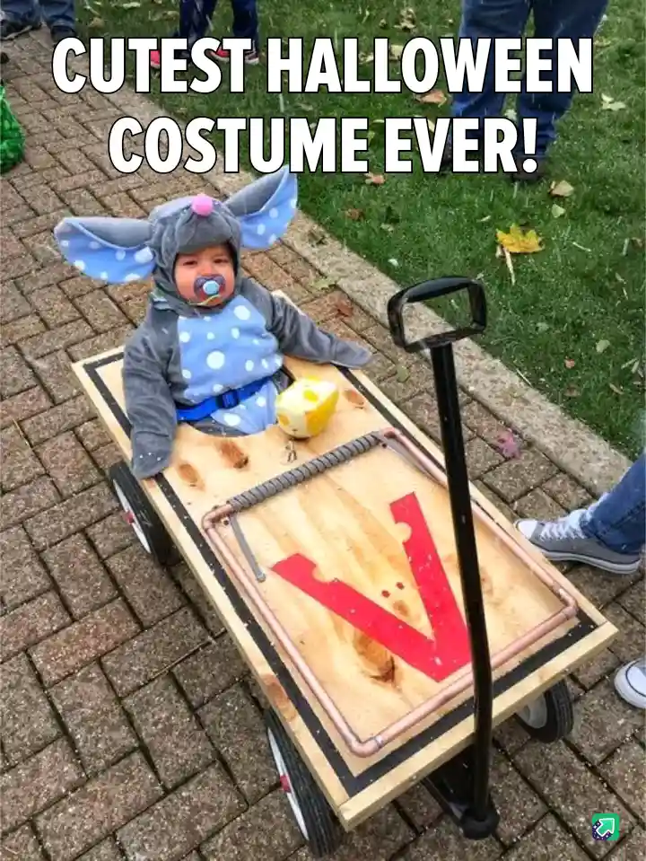 A baby wearing a grey and blue polka-dotted mouse costume with large ears and a pacifier sits in a wooden cart that has been…