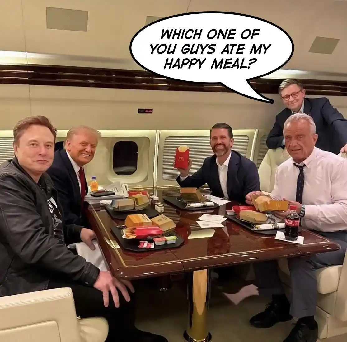 Four men are seated around a polished wooden table inside a private jet, surrounded by McDonald's Happy Meal boxes and…