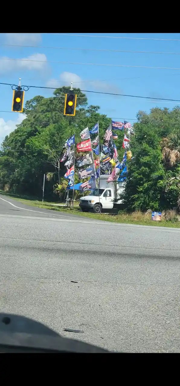 A roadside photo shows two traffic lights both displaying a yellow light above a white truck parked on the shoulder, which…