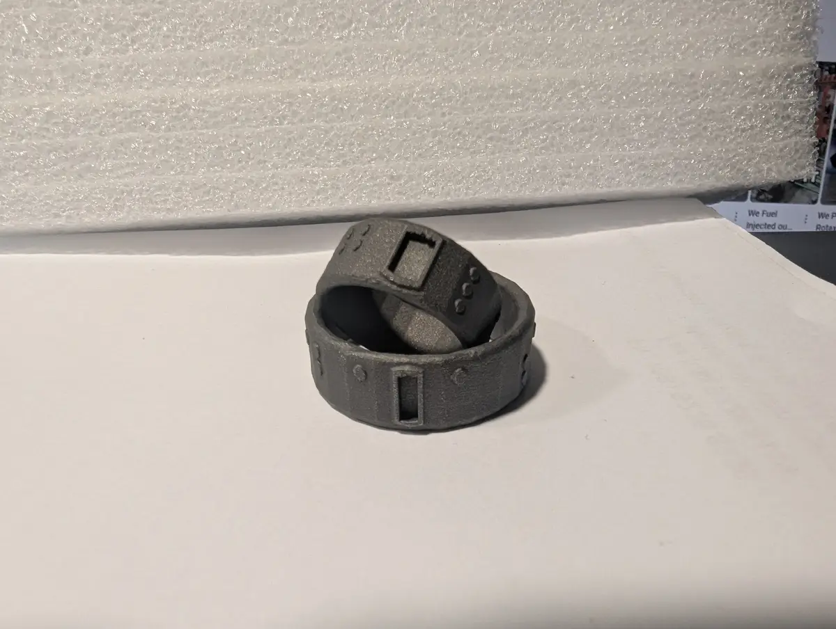 Two gray 3D-printed rings, resembling futuristic or sci-fi tech gear, are stacked on a white surface with bubble wrap in the…