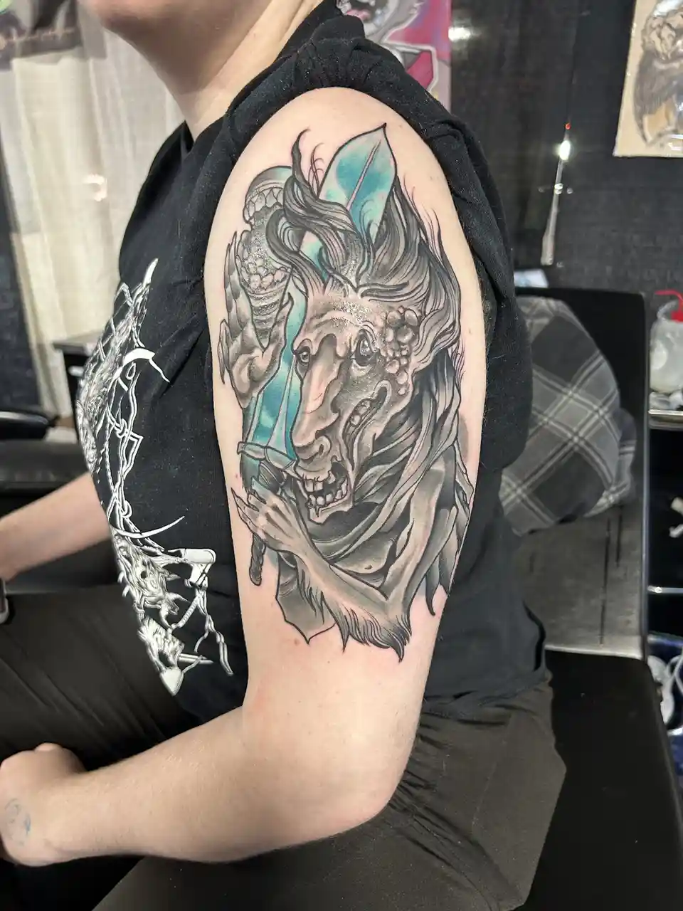 A person wearing a black shirt shows off a large, detailed tattoo on their upper arm depicting a grotesque, screaming…