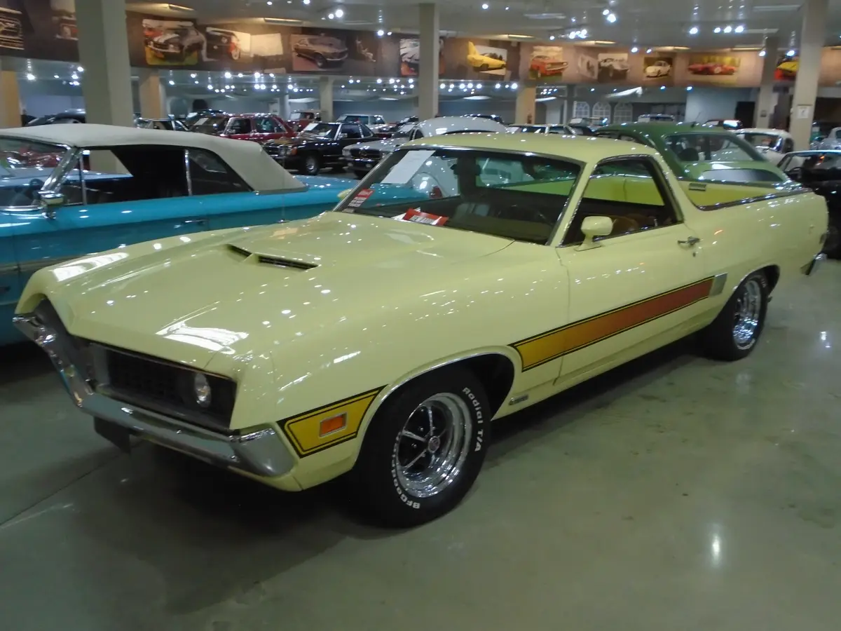 A pale yellow classic American muscle car with a distinctive orange and yellow stripe is displayed in a brightly lit car…