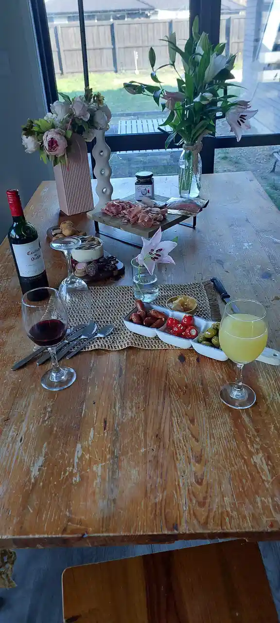 A rustic wooden table is set for a fancy meal with wine, charcuterie, olives, and flowers, but the overlaid text reads 'i'm…