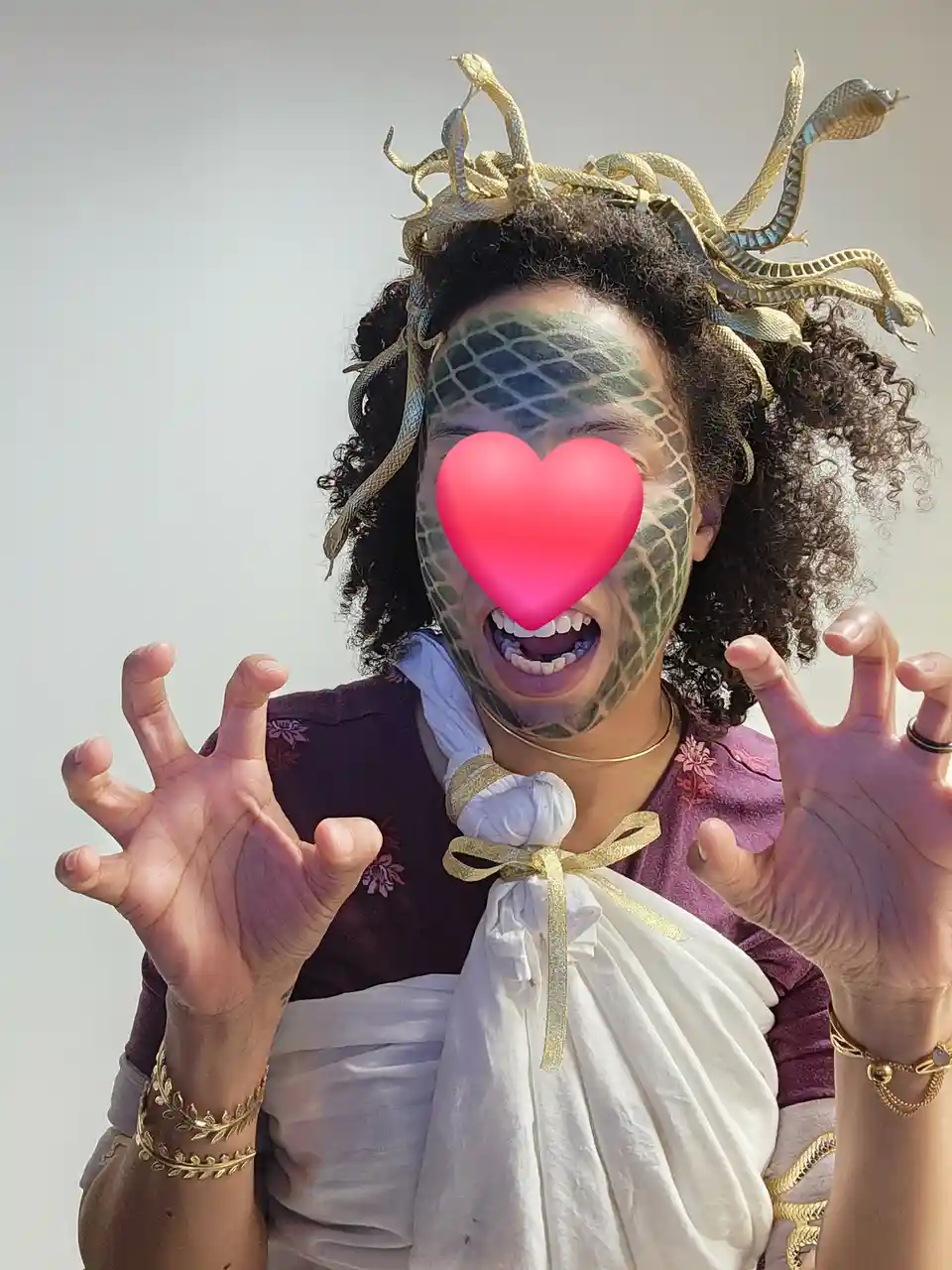 A person dressed as the greek mythological figure medusa, with snakes in their hair and green scales on their face, has a…