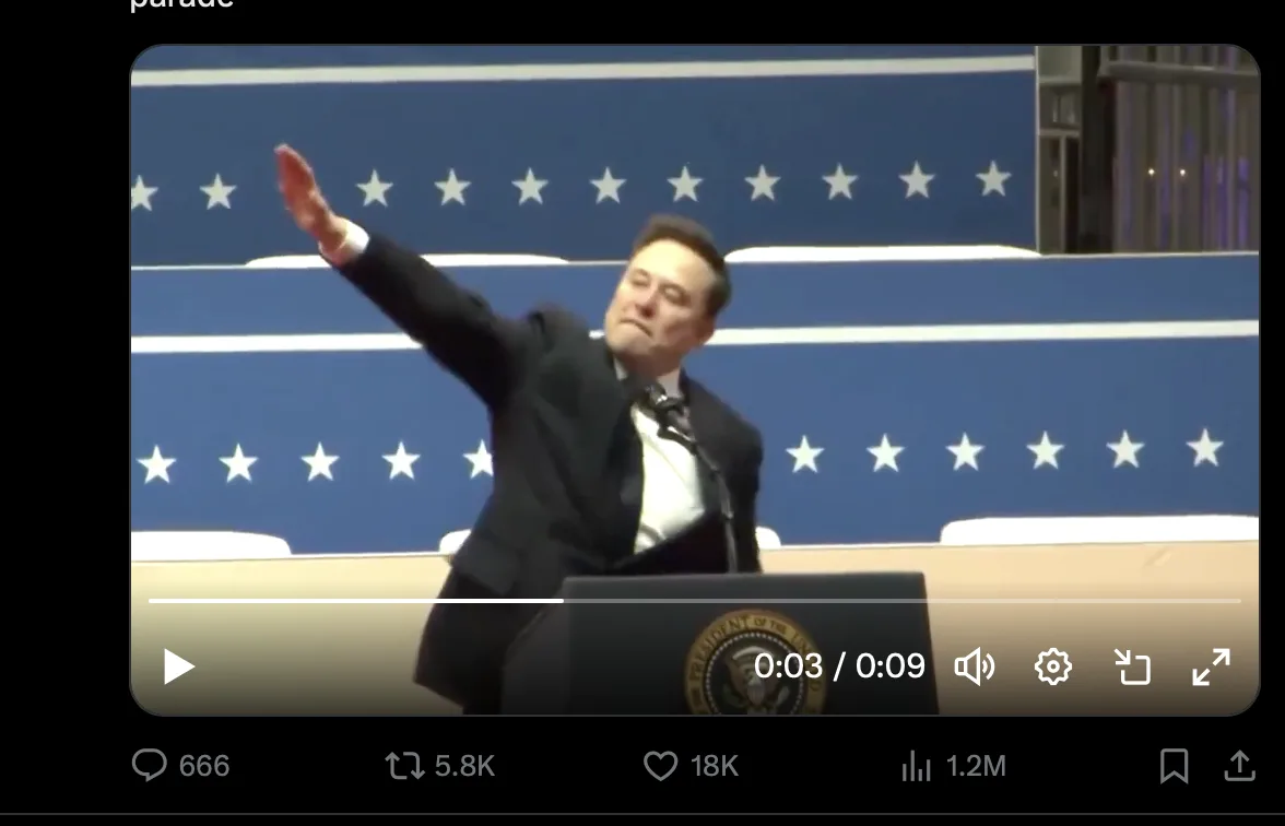A man in a black suit stands at a podium with the presidential seal, raising his right arm in a waving gesture against a…