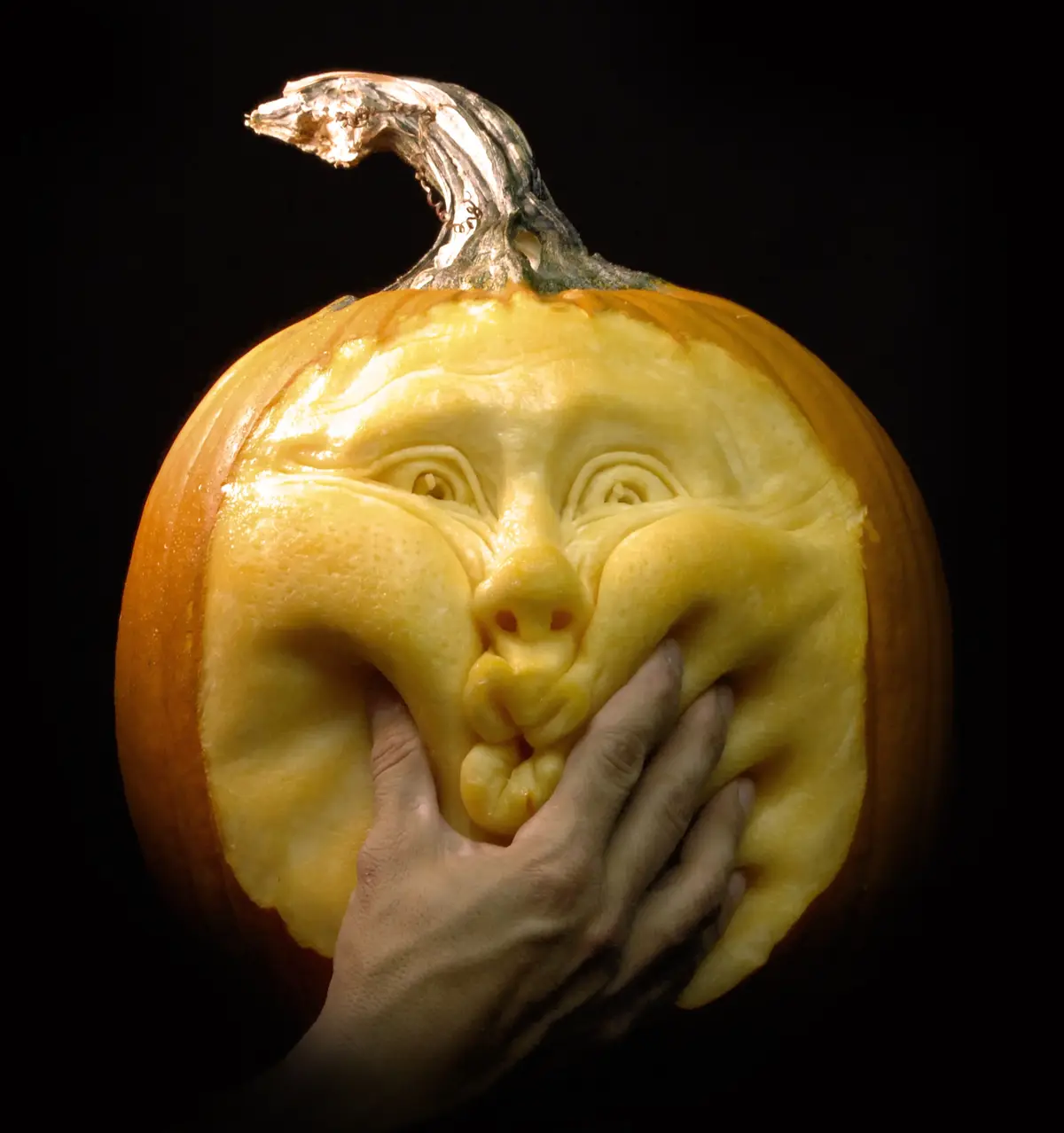 A highly detailed, carved pumpkin with a human-like face, featuring expressive eyes, a nose, and a wide, smiling mouth. A…