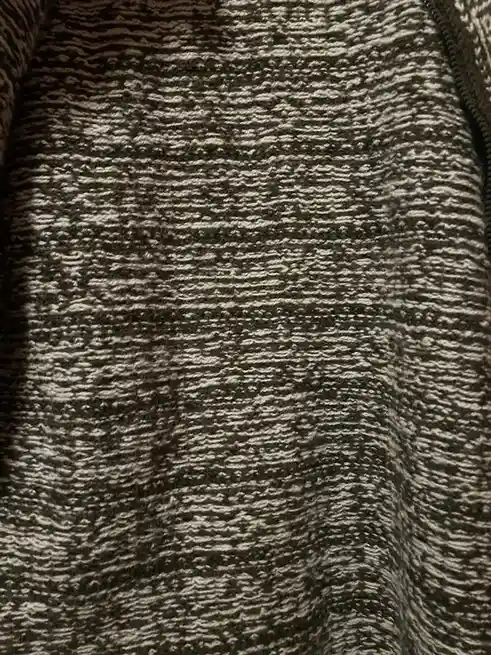 A close-up photo of a dark gray and white speckled knit fabric, likely a sweater, with no visible person or object. The…