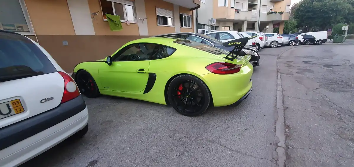 a bright lime green porsche 981 gt4 with black wheels and a rear spoiler is parked in a residential lot next to a white…