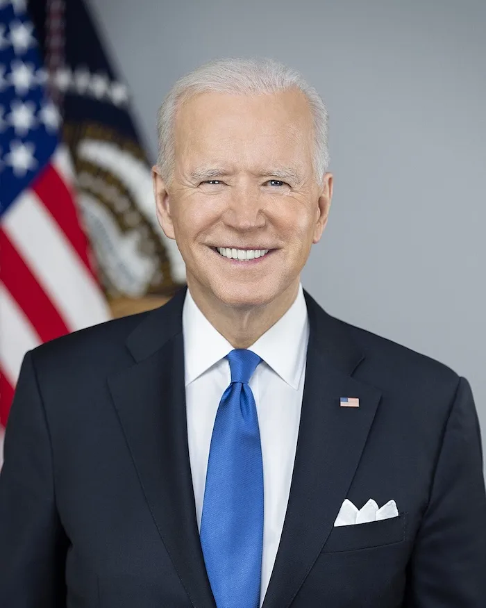 A formal portrait of Joe Biden, the 46th president of the United States, smiling broadly while wearing a dark suit, white…