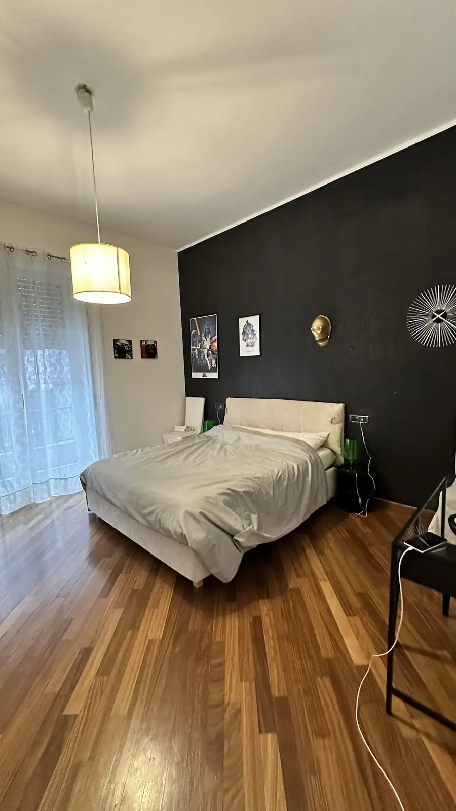 A clean, modern bedroom with hardwood floors, a neatly made bed, and a black accent wall adorned with Star Wars posters and…