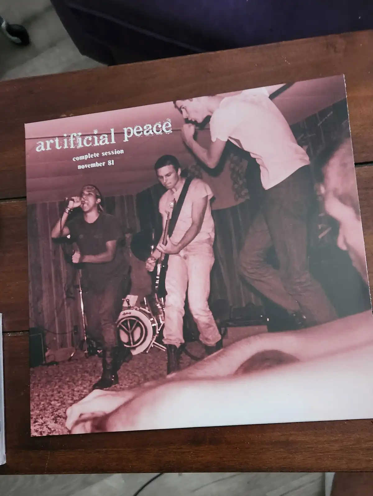 A sepia-toned photo of a band performing live, with a singer, guitarist, and drummer visible on stage. The album cover text…