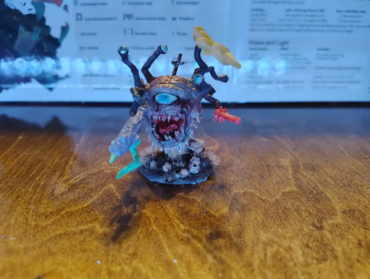 A grotesque, hand-painted miniature monster with one large blue eye, multiple black tentacles with glowing orbs, and a wide…