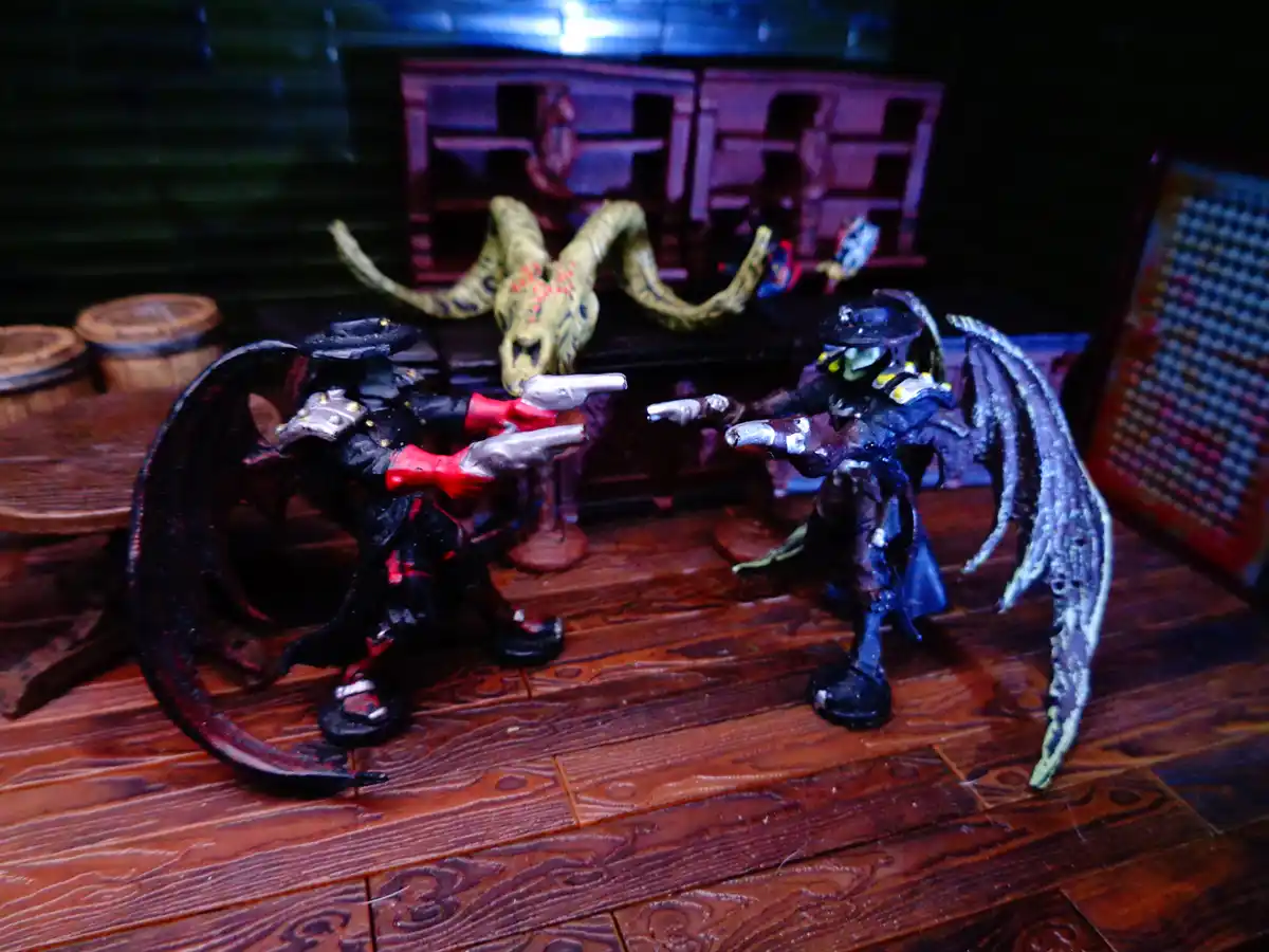 Two painted action figures, resembling demonic or fantasy characters with wings and hats, are posed facing each other with…