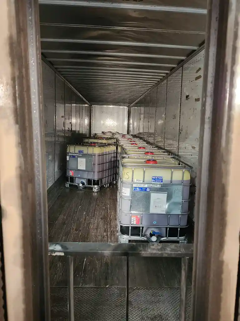 A view from inside a metal trailer looking down a narrow aisle filled with rows of large, identical industrial plastic…