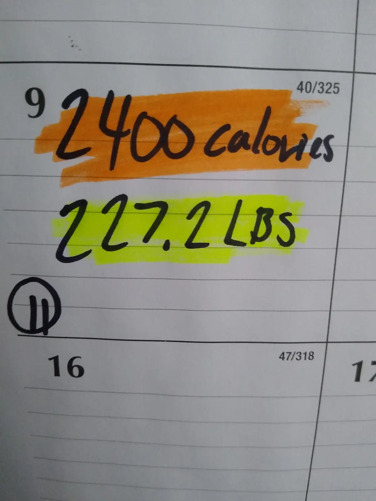 A close-up of a lined notebook page showing handwritten entries: '2400 calories' highlighted in orange and '227.2 LBS'…