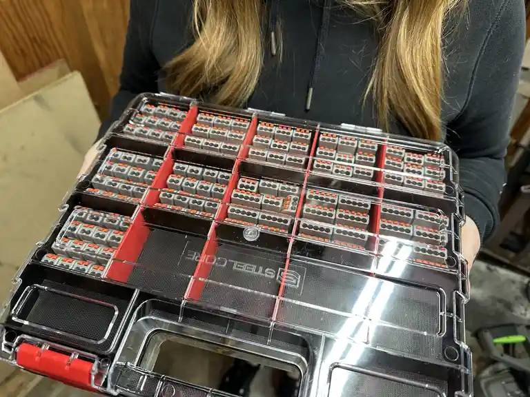 A person holds a clear, red-accented tool case filled with numerous identical gray and orange mechanical keyboard switches…