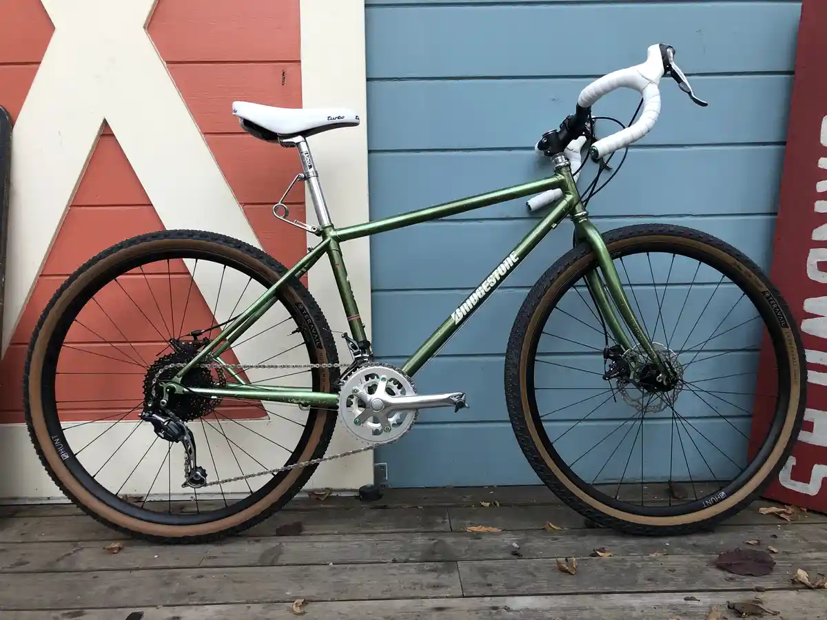 A green bicycle with white handlebars and seat is leaning against a wall with red and blue panels. The bike's frame has the…
