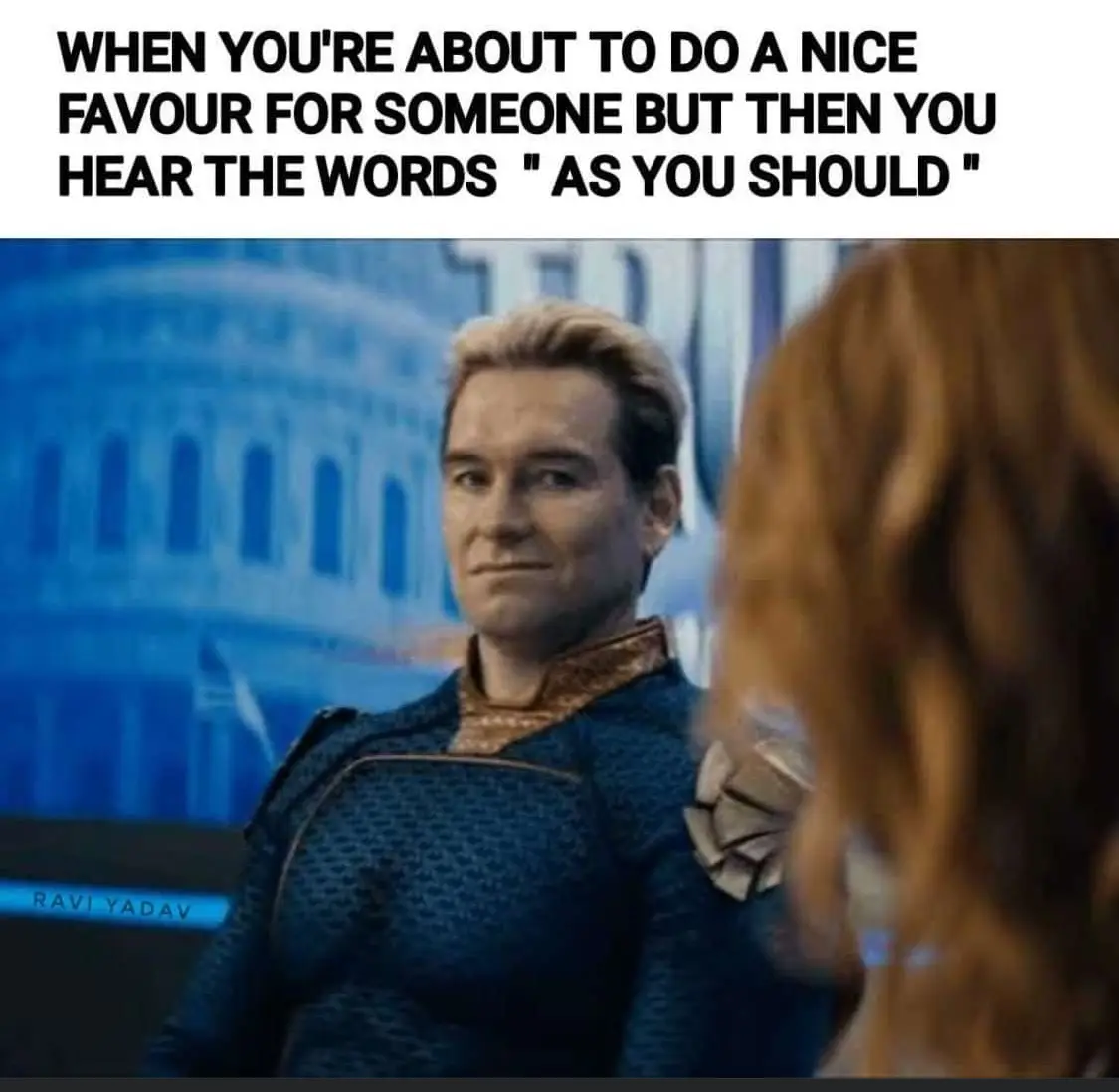 A man in a blue textured superhero costume with a gold collar looks at someone off-screen with a subtle, knowing smirk. The…