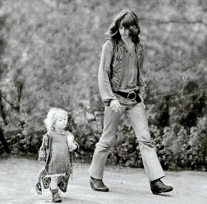 A black-and-white photo shows a young child walking beside a much taller adult man, both looking forward. The child holds a…
