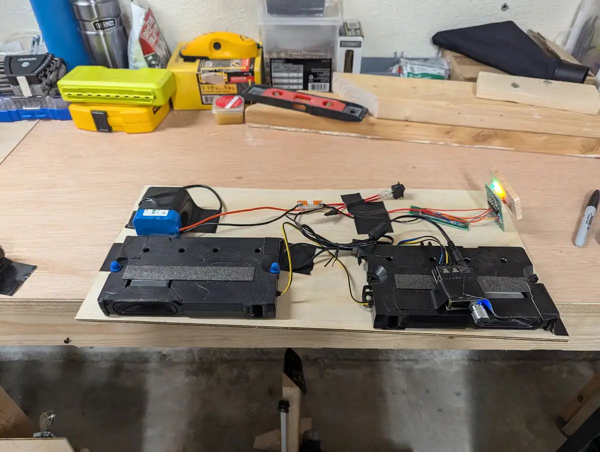 A DIY project on a wooden workbench shows two VHS tape cassettes modified with electronics, wires, and a small circuit board…