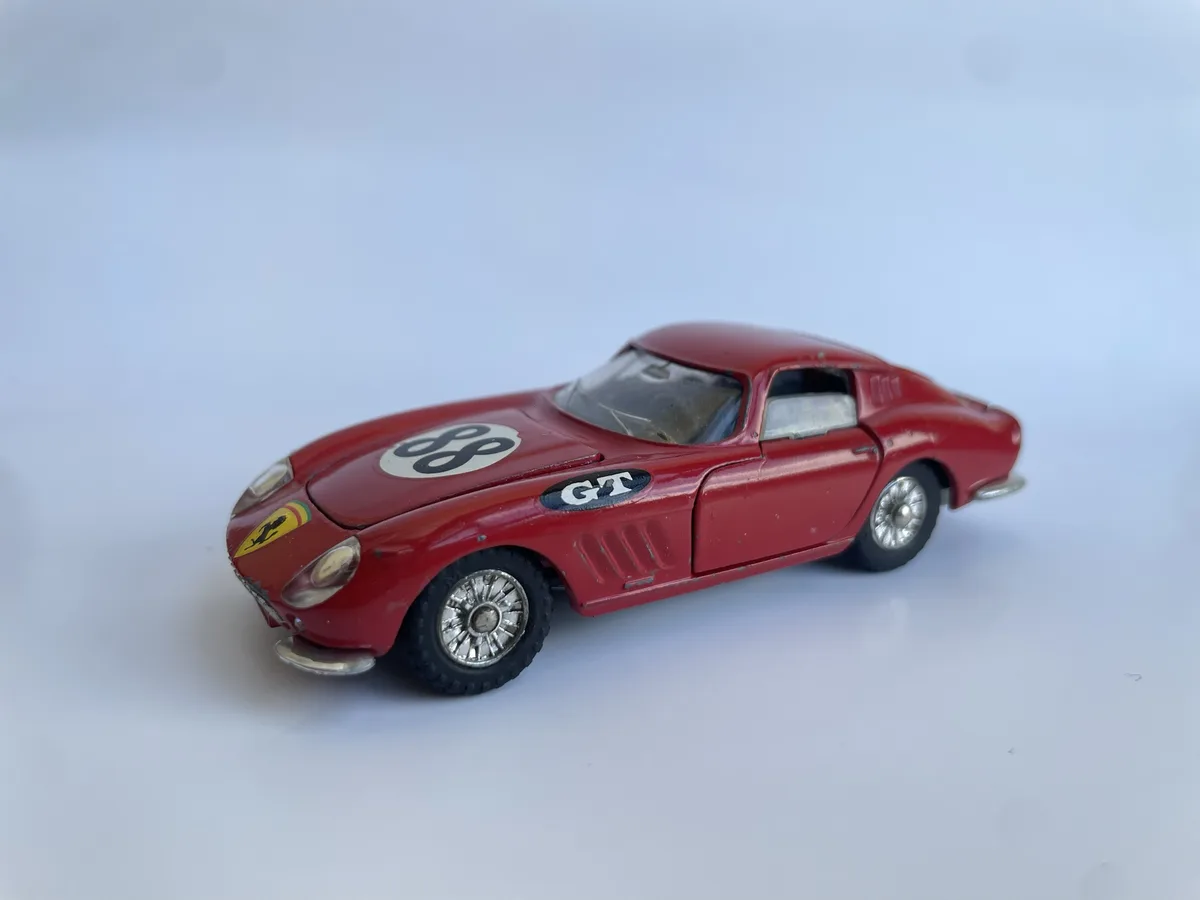 A red vintage toy car, resembling a Ferrari, is shown on a plain white background. It features a yellow Ferrari prancing…
