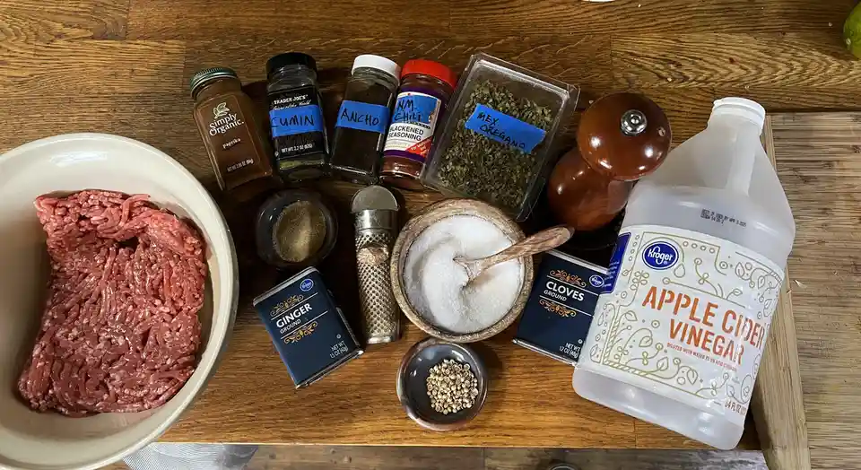 An overhead shot displays a wooden table with ingredients for taco meat: a bowl of raw ground beef, various spices like…