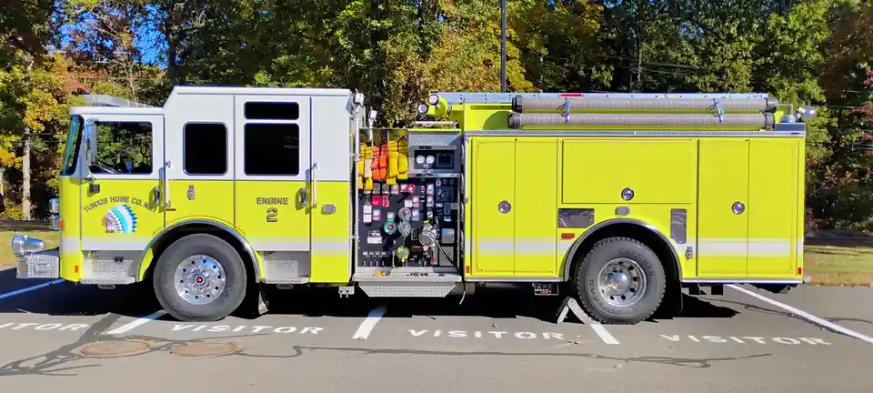 A bright yellow Tunxis Hose Co. No. 1 fire engine, labeled 'ENGINE 2', is parked in a visitor parking spot. Its side panel…