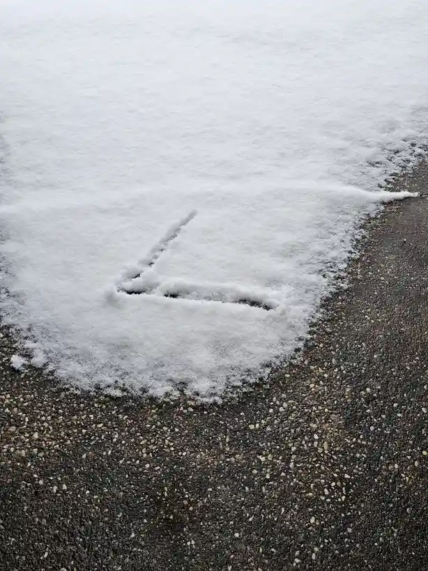 A close-up photo shows a shallow depression in a layer of snow on pavement, shaped like an arrow pointing toward the right…