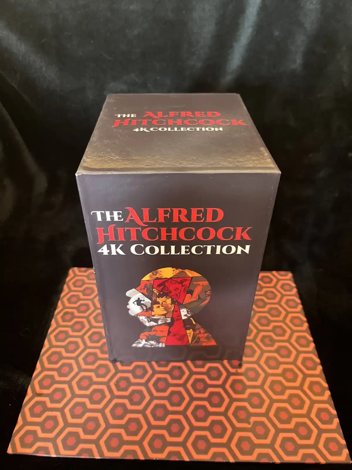 A black box labeled 'The Alfred Hitchcock 4K Collection' sits atop a surface with a distinctive orange and brown hexagonal…