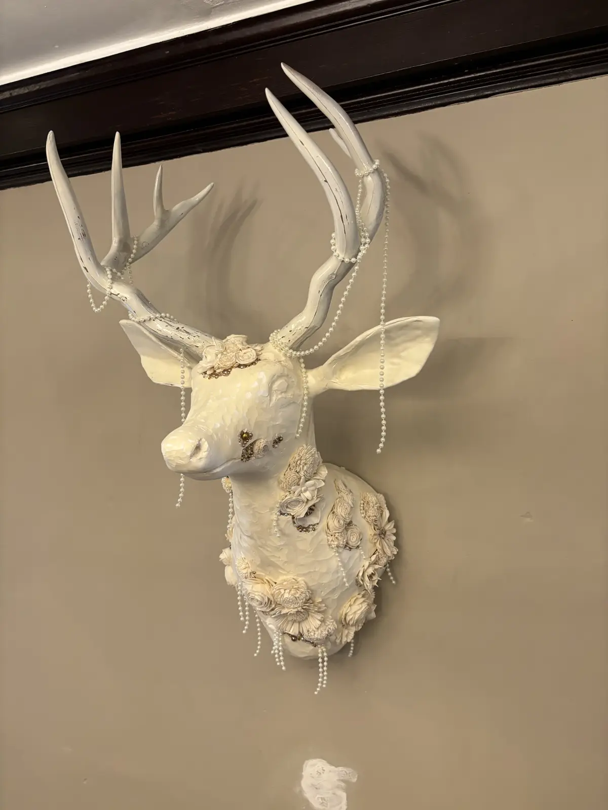A white, ornate deer head mount decorated with pearls and flowers hangs on a beige wall. The overlaid text reads 'i'm not a…