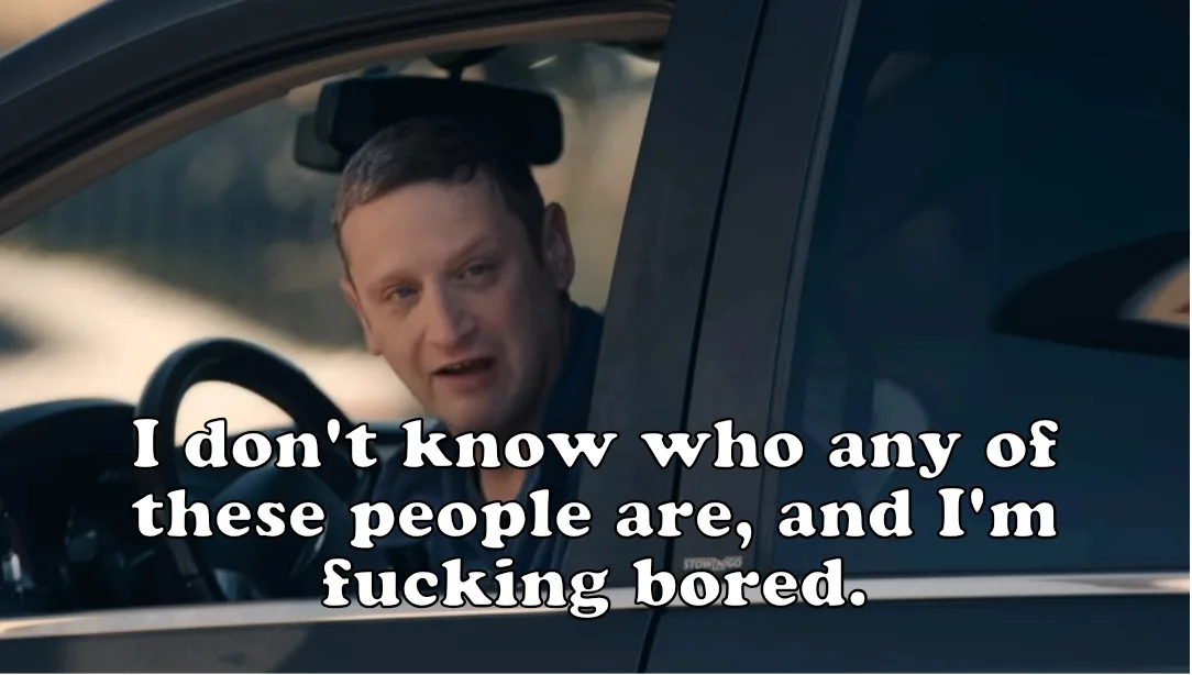 A man sits in the driver's seat of a car, looking out the window with a bored and slightly annoyed expression. White text…