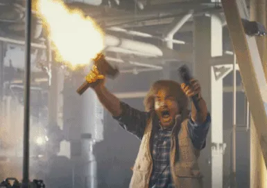 A man with long hair and a vest is shown in six frames inside an industrial setting, holding a flaming torch and a gun…