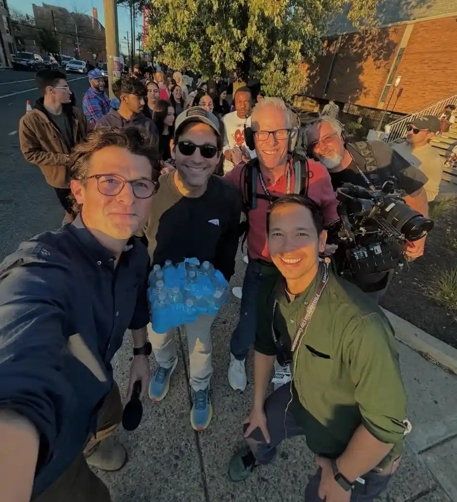 A selfie-style photo shows a group of men, including actor Patrick Dempsey, posing outdoors on a sidewalk with a crowd…