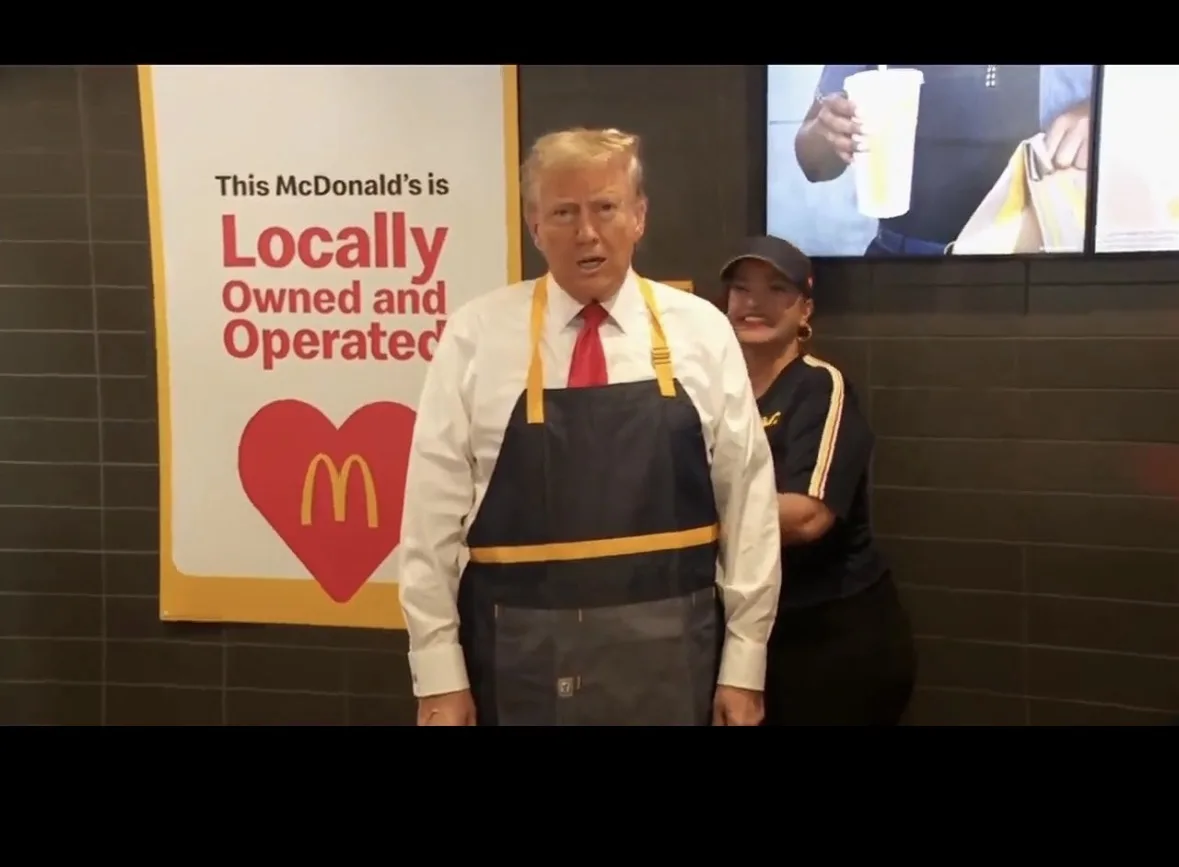 A man in a McDonald's employee apron stands in front of a sign that reads 'This McDonald's is Locally Owned and Operated'…