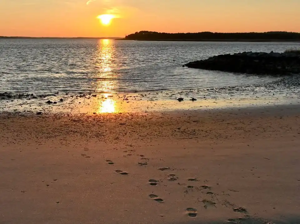 A serene beach sunset with footprints leading toward the water's edge, overlaid with the text 'i walked here, and now i'm…