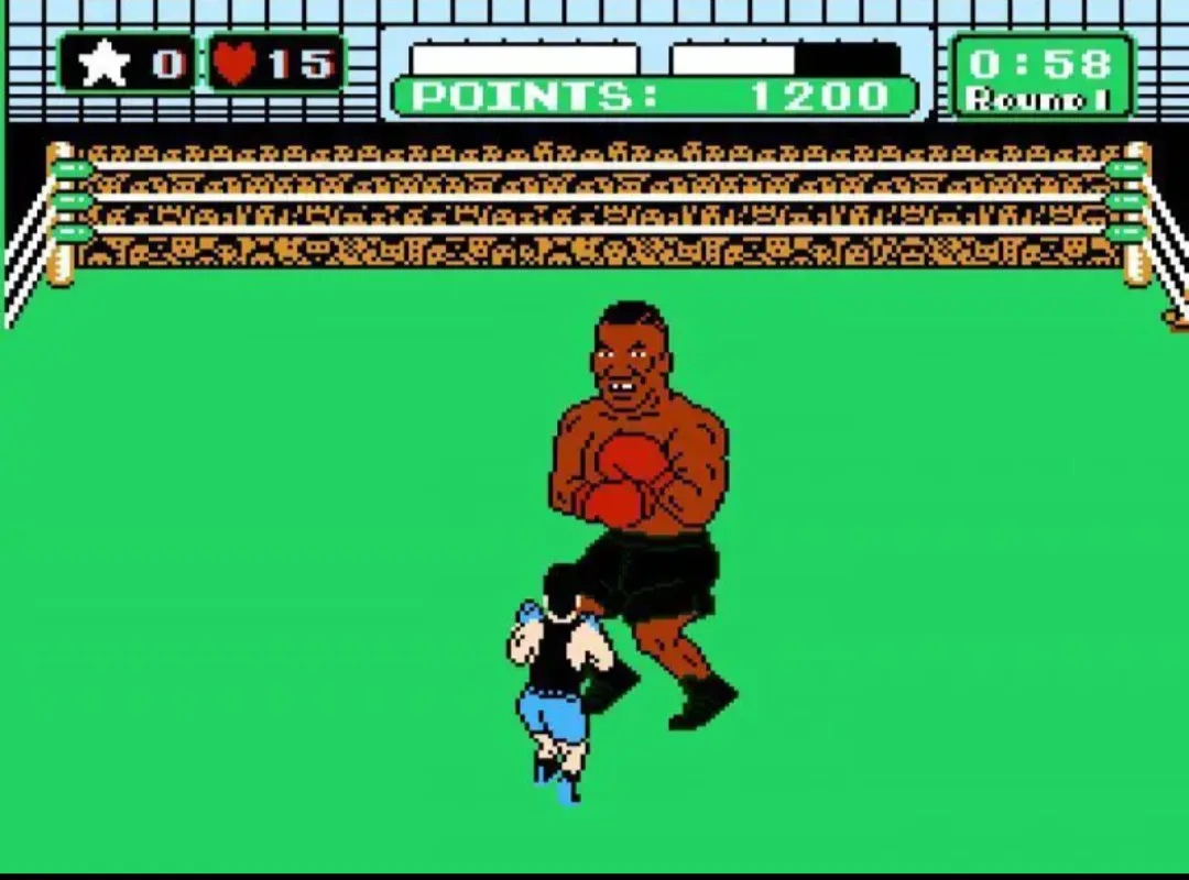 A pixelated video game screenshot from a retro boxing game shows a large, muscular boxer in red gloves standing over a…