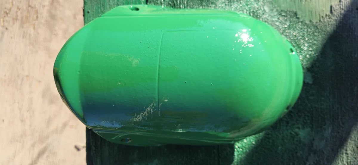 A close-up photo shows a glossy, bright green, oval-shaped object, likely a piece of machinery or equipment, mounted on a…