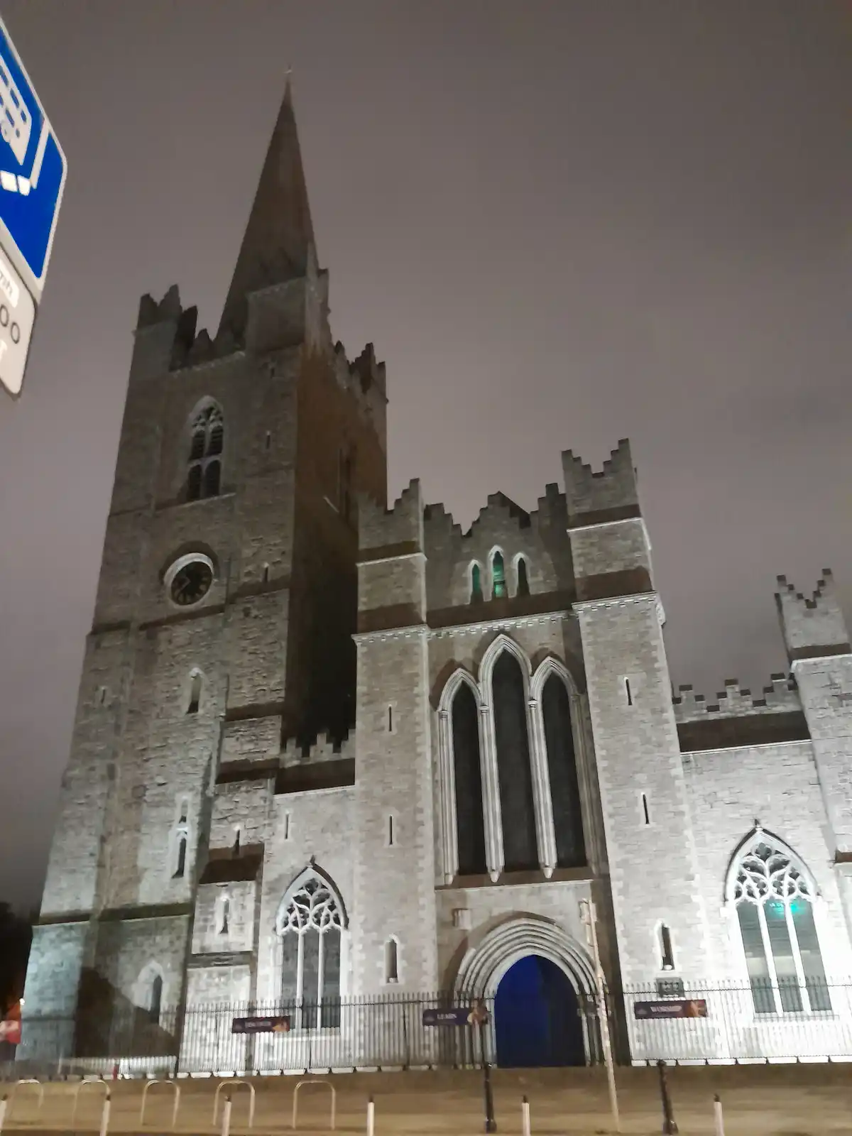 A nighttime photo of a large, illuminated Gothic-style stone church with a tall spire and arched windows, featuring overlaid…